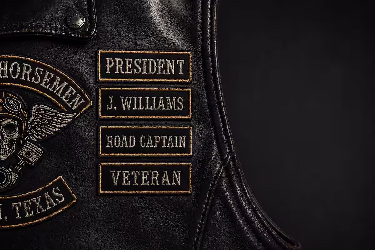 Close-up of a leather motorcycle vest displaying embroidered custom rank and name patches on the chest.