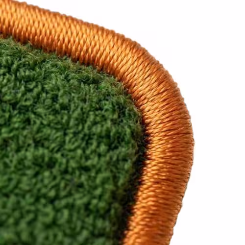 Macro view of a fluffy green chenille patch featuring a thick, shiny orange stitched merrow border.