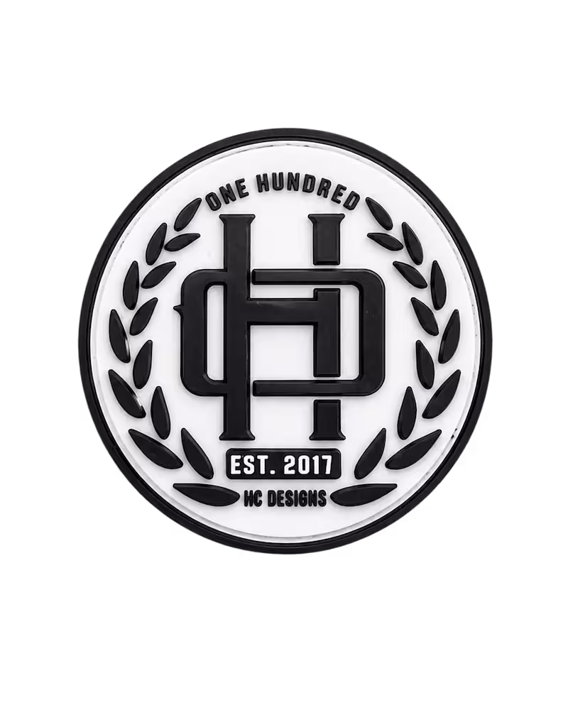 Circular black and white 3D PVC patch with a laurel wreath and raised HC Designs monogram.
