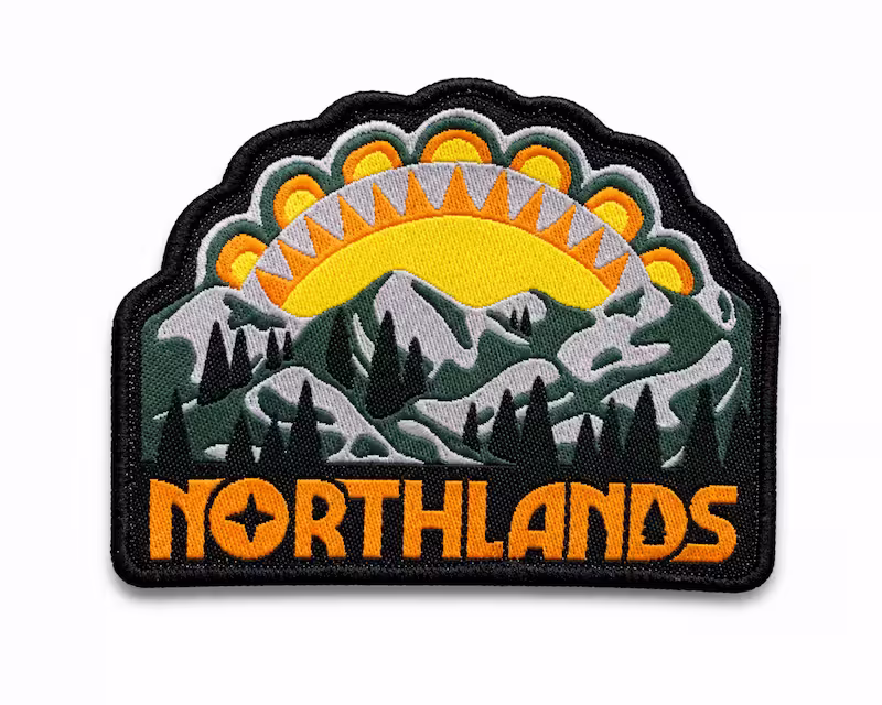 Custom shaped woven patch depicting a mountain landscape with pine trees a yellow sun, and Northlands.