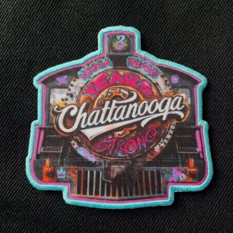 High-resolution printed patch with complex graphics and a teal embroidered border on a black canvas texture.