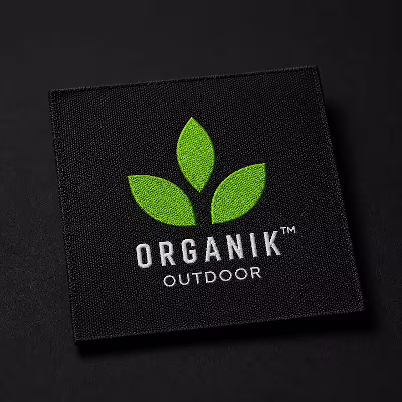 Square black woven patch featuring three green leaves and the Organik Outdoor logo in white text